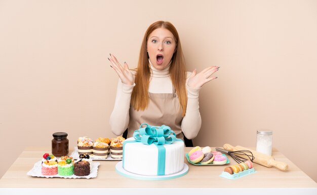 Giovane donna rossa con una grande torta con sorpresa espressione facciale