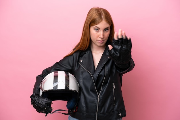 Young redhead woman with a motorcycle helmet isolated on pink\
background making stop gesture