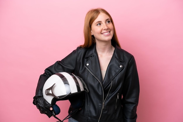 Young redhead woman with a motorcycle helmet isolated on pink background thinking an idea while looking up