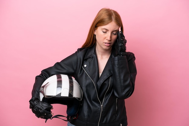 Молодая рыжая женщина в мотоциклетном шлеме на розовом фоне с головной болью