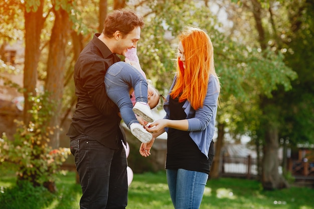 A young redheaded mother plays in the park with her husband and their little daughter