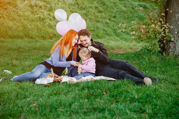 A young redheaded mother sitting in the park with her husband and their little daughter