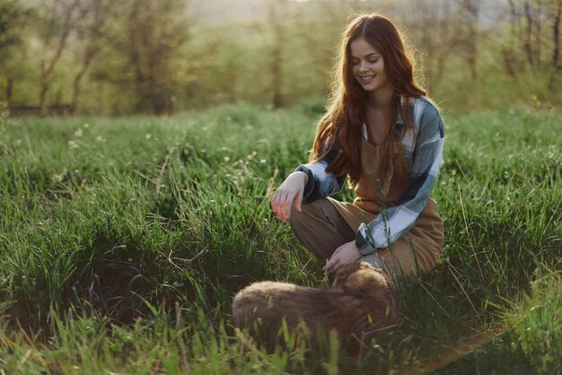 Young redheaded woman playing in nature with her dog in sunny park at sunset in summer