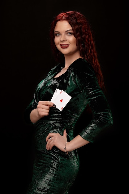 Giovane donna dai capelli rossi in posa con carte da gioco in mano, su sfondo nero