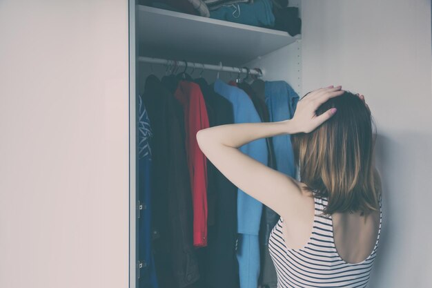 Молодая рыжая девушка выбирает одежду в гардеробе.