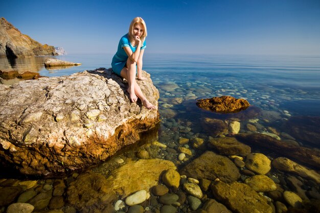 Young relaxed caucasian woman sits on a stone and enjoys the rays of the summer sun