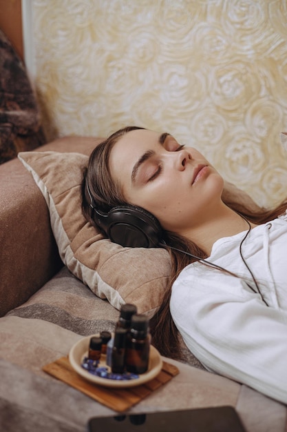 Молодая расслабленная женщина слушает музыку с закрытыми глазами и лежит на кровати во время медитации