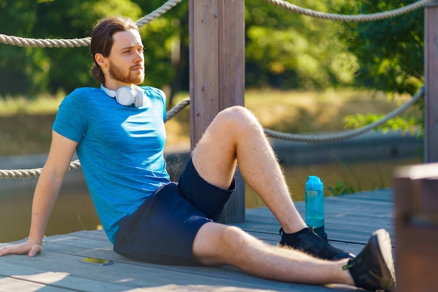 Giovane uomo sportivo rilassato che si rilassa dopo l'allenamento mattutino all'aperto nella natura