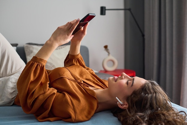 Young relaxed woman with earphones looking at smartphone screen