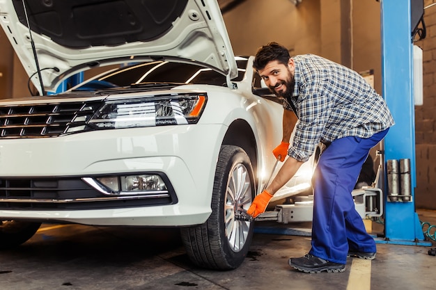 Young repairman fixing tire on the car and smiling at front