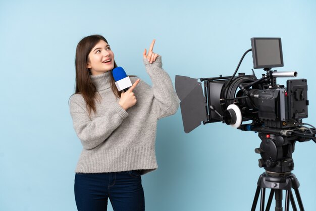 Молодая женщина репортера держа микрофон и сообщая новости указывая указательным пальцем отличная идея