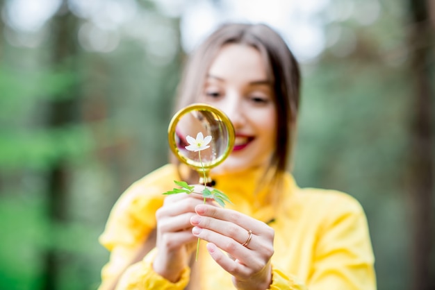 Young researcher looking on the flower through the magnifying glass in the forest