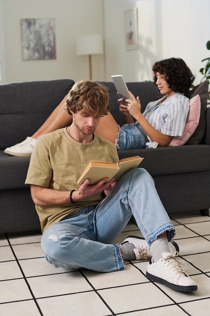 Young restful man and woman reading book and watching online movie