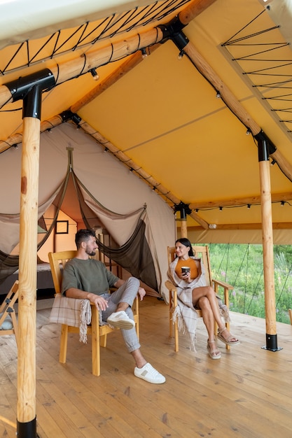 Young restful man and woman relaxing in armchairs by glamping house