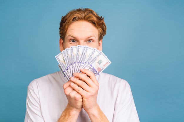 young rich red haired man in casual holding money dollar bills with surprise