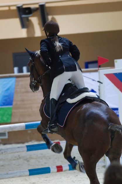 Young rider on black horse galloping at show jumping competition