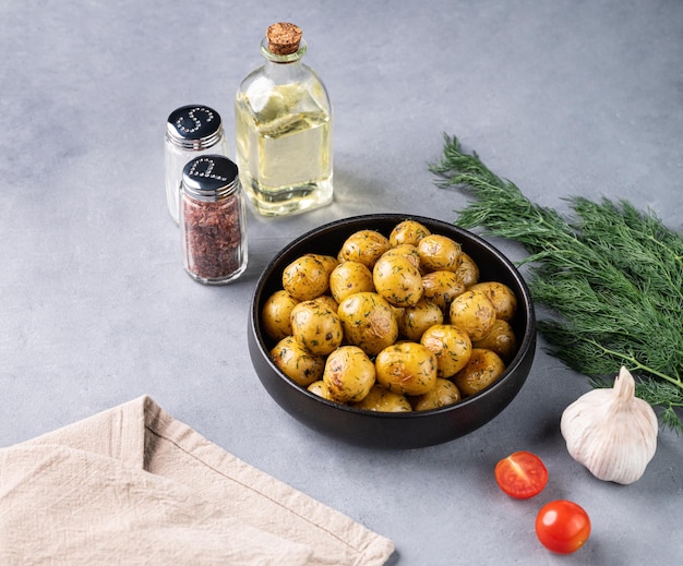 Young roasted baby potatoes in a black pan with tomatoes oil garlic and herb on a blue background