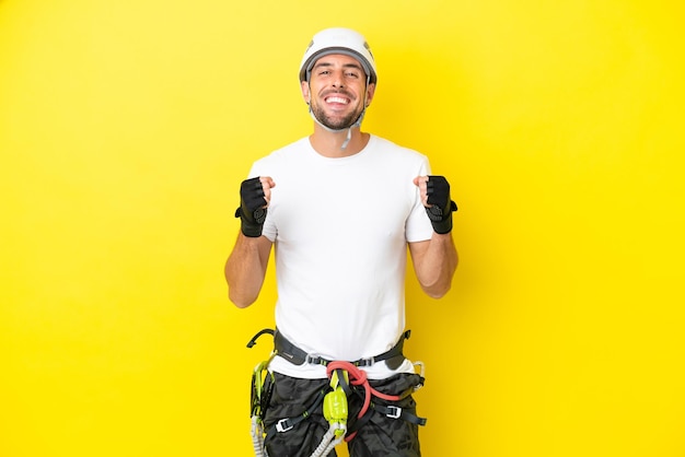 Young rock climber man isolated on yellow background celebrating a victory in winner position