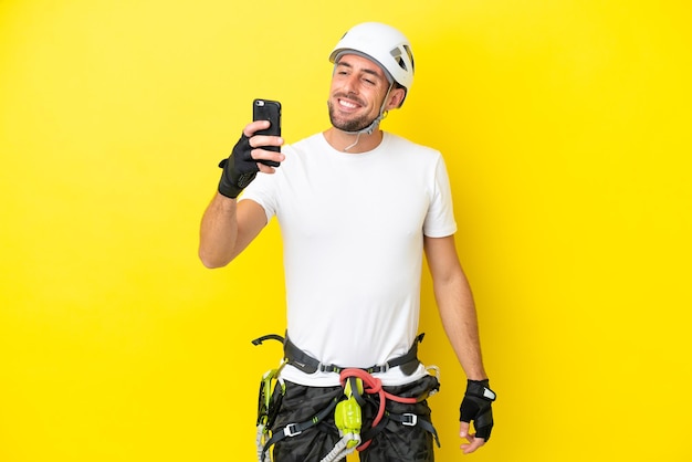 Young rock climber man isolated on yellow background making a selfie