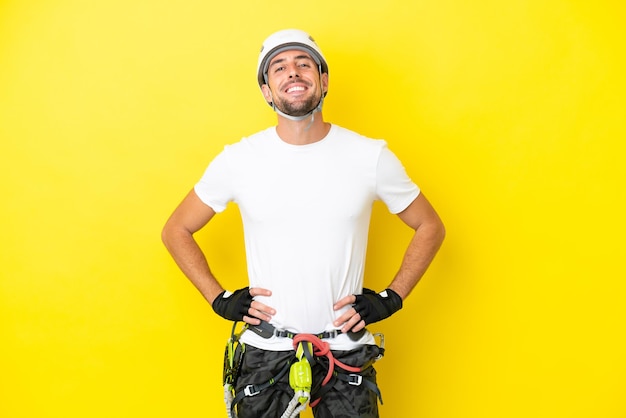 Young rock climber man isolated on yellow background posing\
with arms at hip and smiling