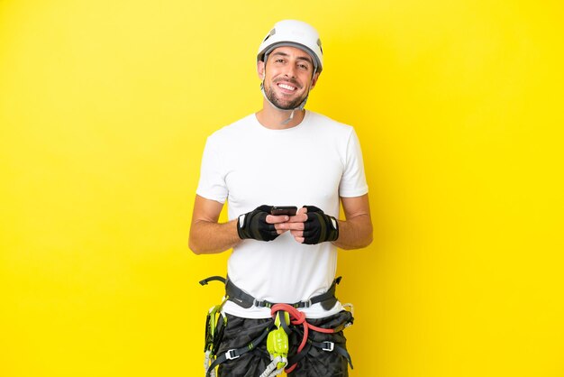 Photo young rock- climber man isolated on yellow background sending a message with the mobile