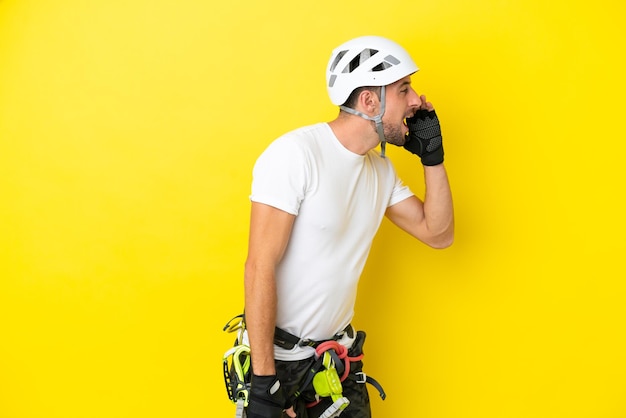 Young rock climber man isolated on yellow background shouting with mouth wide open to the lateral