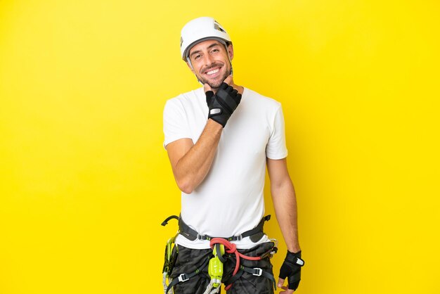 Young rock climber man isolated on yellow background smiling