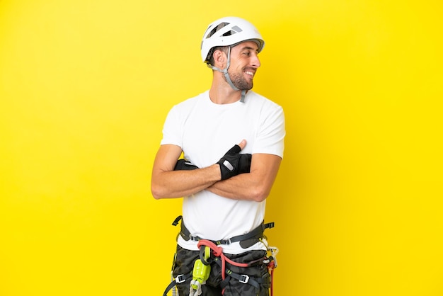 Young rock- climber man isolated on yellow background with arms crossed and happy