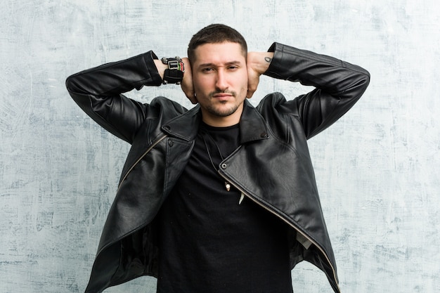 Young rocker man covering ears with hands trying not to hear too loud sound.