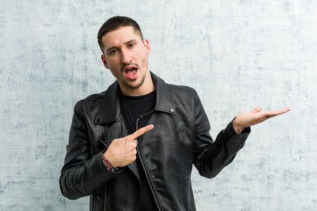 Young rocker man excited holding a copy space on palm.