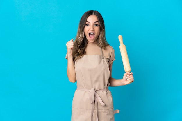 Young Romanian woman holding a rolling pin on blue celebrating a victory in winner position