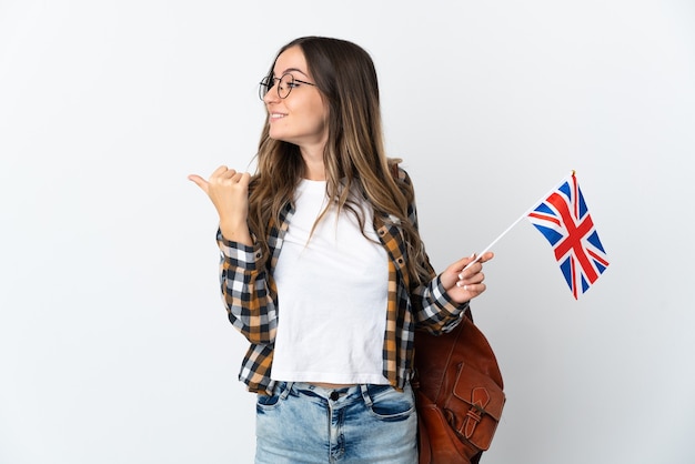 Young Romanian woman holding an United Kingdom flag isolated on white background pointing to the side to present a product