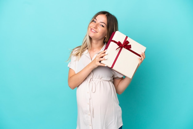 Young Romanian woman isolated on blue background pregnant and holding a gift