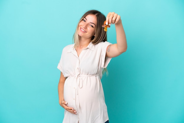 Young Romanian woman isolated on blue background pregnant and holding a pacifier