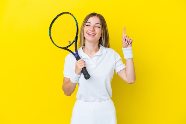 Young Romanian woman isolated on yellow background playing tennis and pointing up