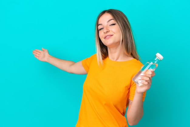 Young Romanian woman with a bottle of water isolated on blue background extending hands to the side for inviting to come