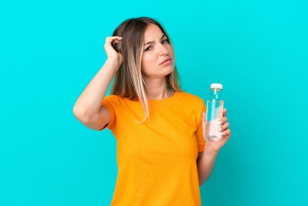 Young Romanian woman with a bottle of water isolated on blue background having doubts