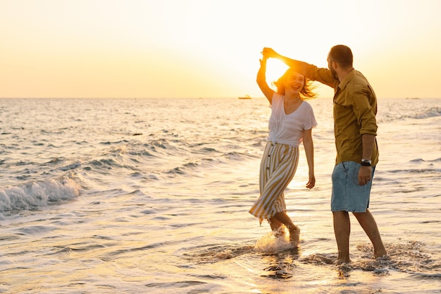 Giovane coppia romantica che balla girando intorno al mare vista sul mare al tramonto con un bel cielo coppia romantica sulla spiaggia al tramonto dorato coppia di innamorati che si divertono sulla spiaggia