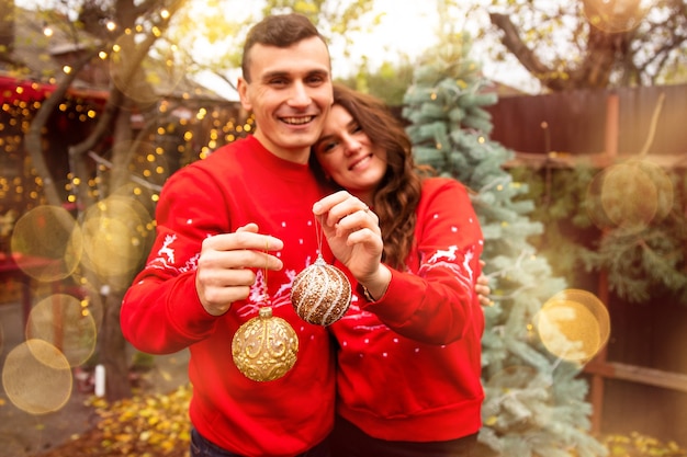 나무에 공을 들고 배경에 포옹 하는 젊은 로맨틱 커플. 그들은 크리스마스 전에 야외에서 크리스마스 트리를 장식합니다.