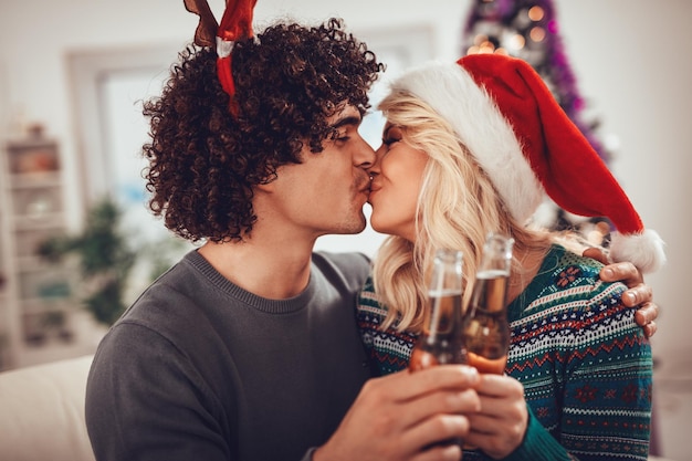 Young romantic couple hugging and kissing in Christmas time. They are toasting with bottles of drink.