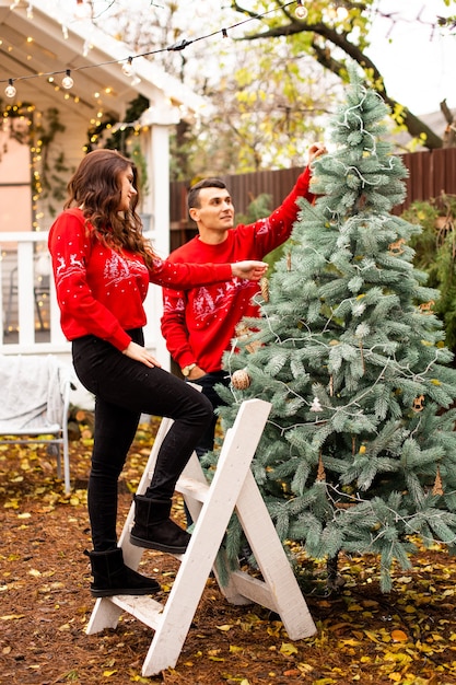 Young romantic couple is decorating Christmas tree outdoors before Christmas. Enjoying spending time together in New Year Eve.