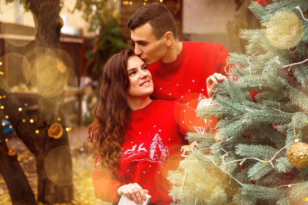 Young romantic couple is decorating Christmas tree outdoors before Christmas. Enjoying spending time together in New Year Eve.