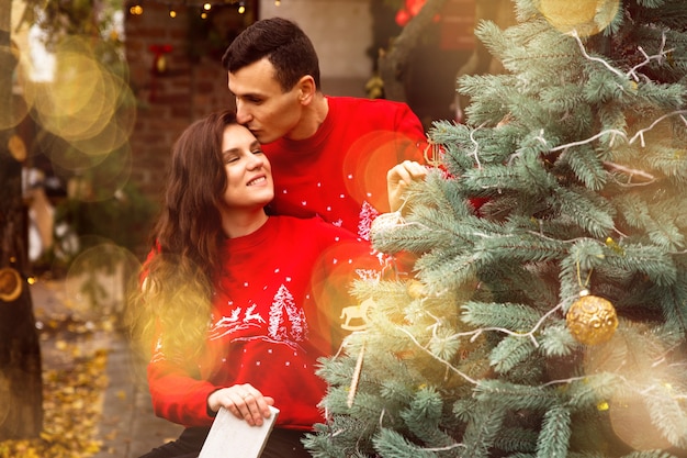 Photo young romantic couple is decorating christmas tree outdoors before christmas. enjoying spending time together in new year eve.