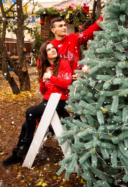 Young romantic couple is decorating Christmas tree outdoors before Christmas. Enjoying spending time together in New Year Eve.