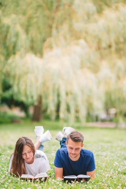 Young romantic couple lying in park and reading books