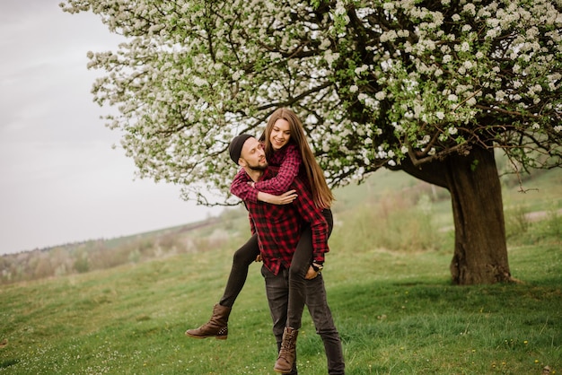Young romantic couple walking on the meadow and blooming tree and have fun