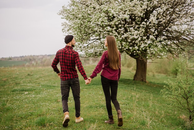 Young romantic couple walking on the meadow and blooming tree and have fun