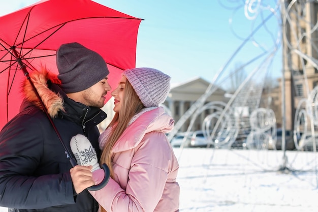 Young romantic couple with bright umbrella on sunny winter day