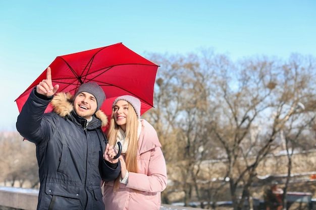 Young romantic couple with bright umbrella on sunny winter day