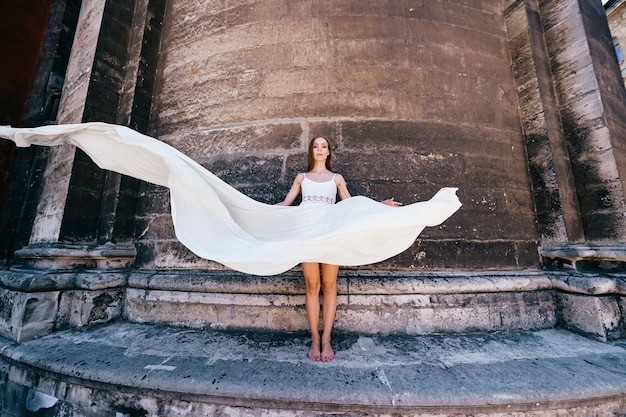 写真 石の古代の壁を越えてポーズをとる長い白い流れるようなドレスの若いロマンチックなエレガントな女の子
